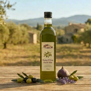 Une bouteille d'« Huile d'Olive Fruité Mûr » artisanale posée sur une table en bois avec quelques olives fraîches, une figue et de la lavande, devant une oliveraie ensoleillée.